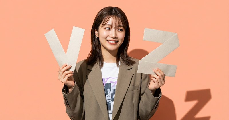 V型とZ型のDMを両手で持ち、笑顔で見比べる日本人女性