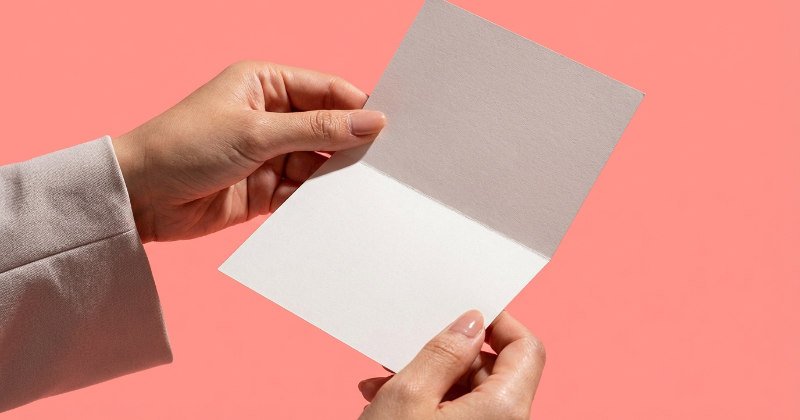 シンプルなV型DMを少し開いて見せている日本人の手元のクローズアップ